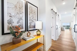 A hallway with artwork, a vase with flowers, a lamp, and a bookshelf.