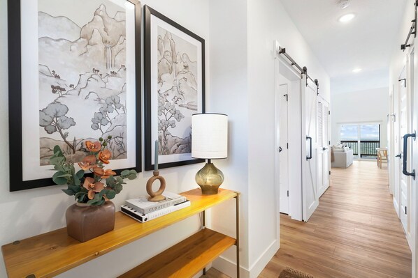 A hallway with artwork, a vase with flowers, a lamp, and a bookshelf. - Private Hot Tub, Stunning Decor & Panoramic Lake Views with Free SDC Tickets (Kimberling City)