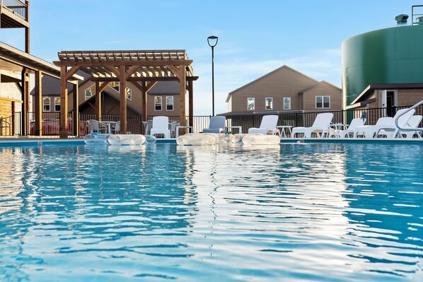 A swimming pool with lounge chairs, a wooden pergola, and a large water tank. - Private Hot Tub, Stunning Decor & Panoramic Lake Views with Free SDC Tickets (Kimberling City)
