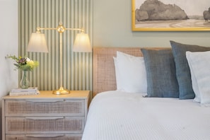 A neatly made bed with white bedding, a bedside lamp, a small bedside table with a vase of flowers, and a framed landscape painting on the wall. - Private Hot Tub, Stunning Decor & Panoramic Lake Views with Free SDC Tickets (Kimberling City)