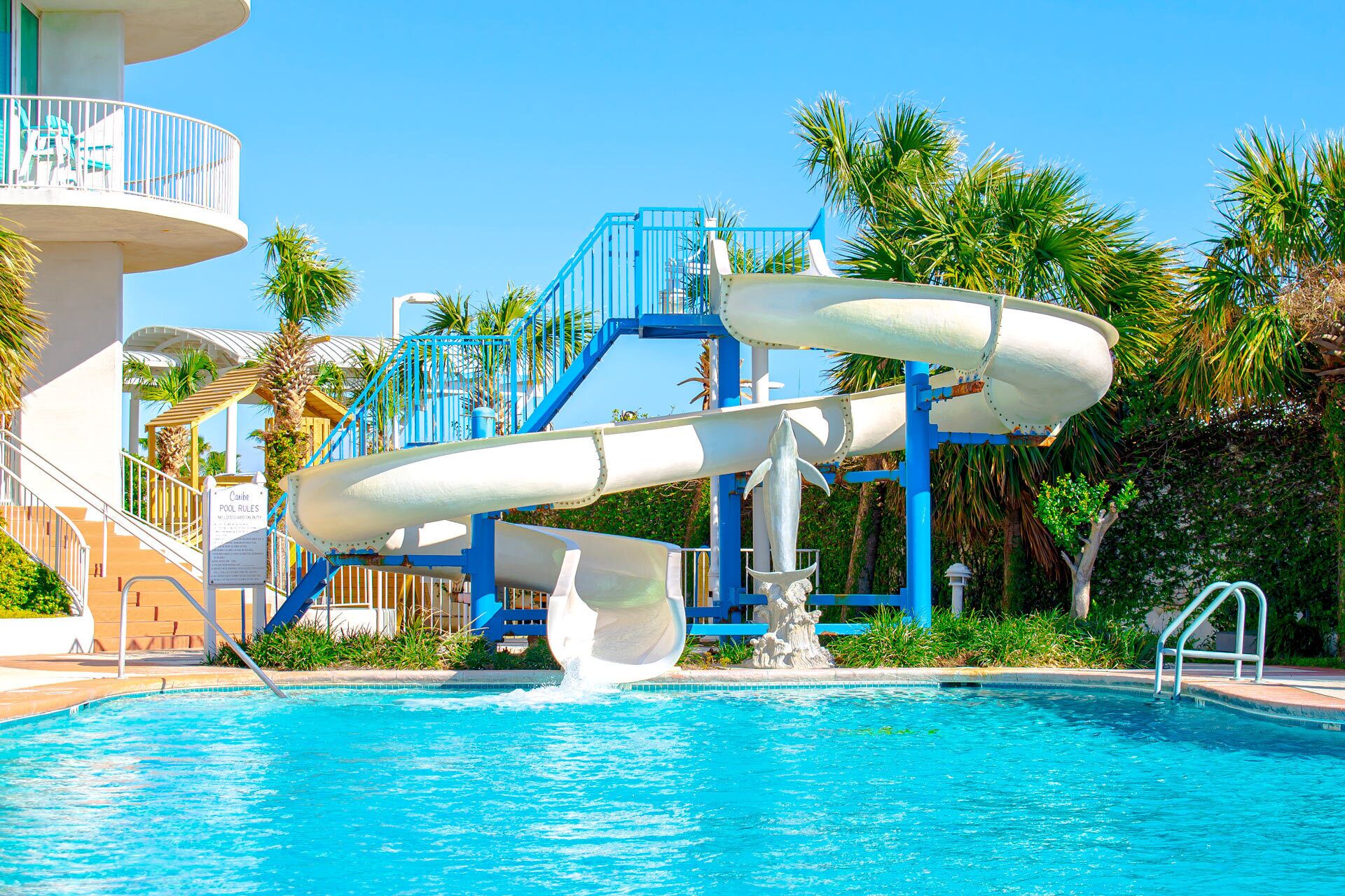 A pool with two water slides, a lifeguard tower, and palm trees.