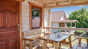 Una terraza de madera con un banco y una mesa, una puerta de madera y vistas a una casa con tejado de tejas.