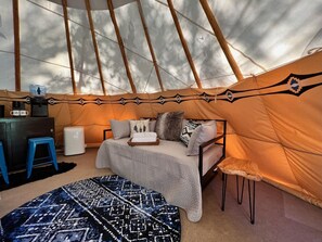 Een gezellig interieur van een tent met een bed, een klein tafeltje en een stoel.