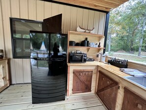 Een kleine keuken met een zwarte koelkast, houten kastjes en een magnetron op een houten aanrecht.