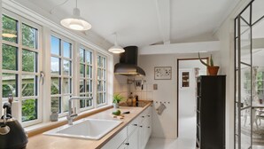 A modern kitchen with large windows, a central island, and a black range hood. - 3 bedroom stunning home in Græsted (Græsted)
