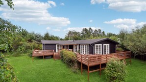 A wooden cabin with a deck, surrounded by lush greenery and trees. - 3 bedroom stunning home in Græsted (Græsted)