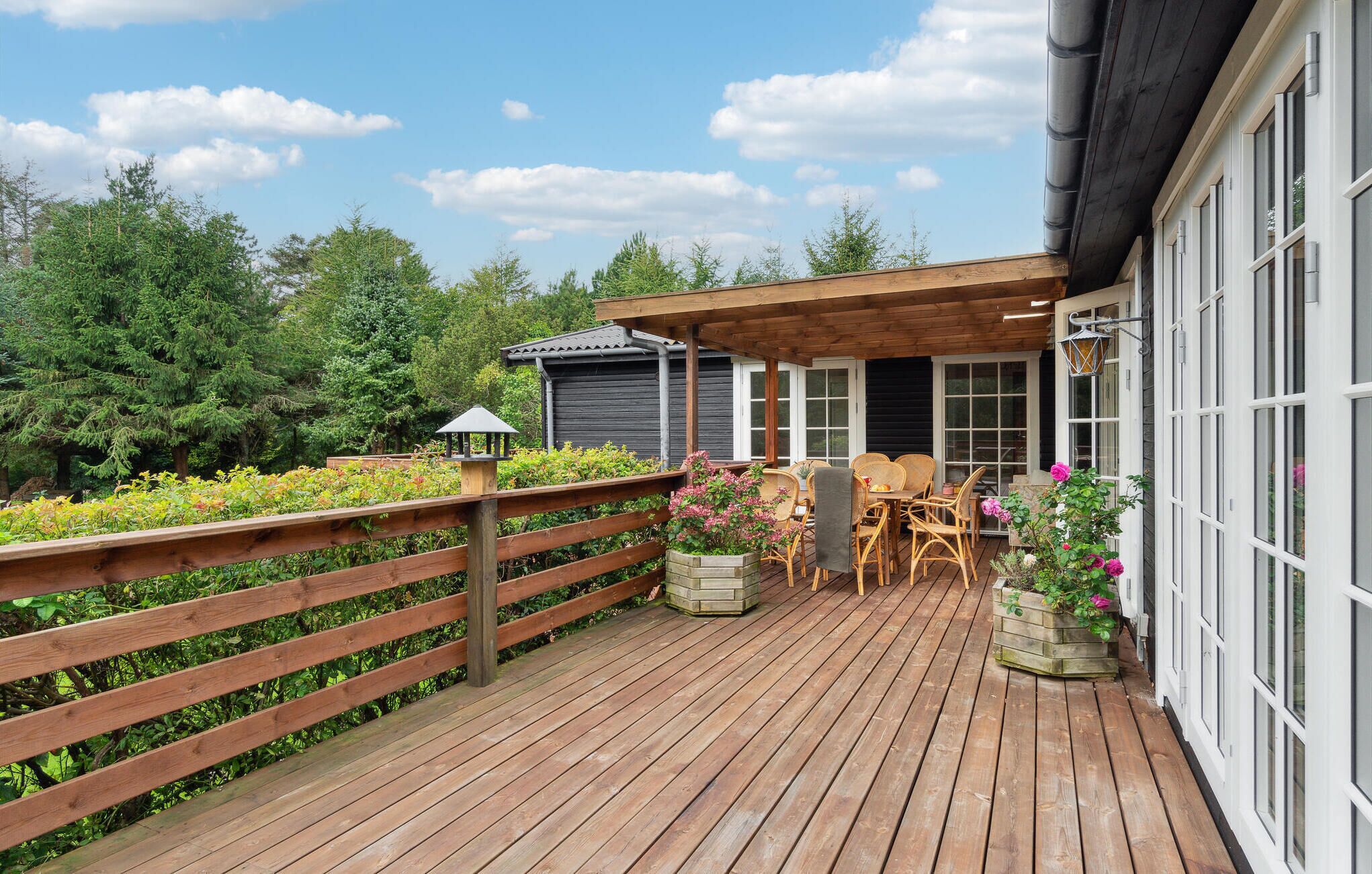 A wooden deck with outdoor furniture, a pergola, and a garden area with flowers and shrubs.