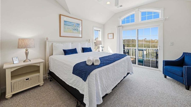 Une chambre avec un grand lit, un ventilateur de plafond, un balcon avec vue et une chaise bleue.