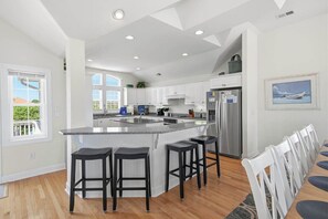 Una cocina moderna con una isla central, taburetes de bar y un comedor con sillas blancas.