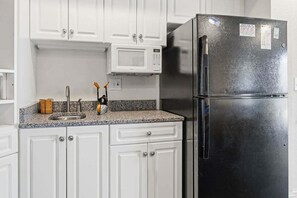 Una cocina con armarios blancos, un refrigerador de acero inoxidable, un microondas y una encimera de granito.