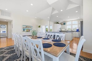 Una cocina moderna con armarios blancos, una isla central y una zona de comedor con sillas blancas y una mesa de madera.