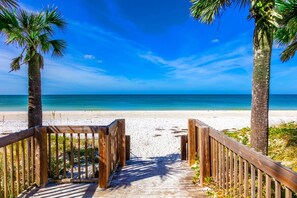 Un sendero de madera que conduce a una playa con palmeras y un cielo azul despejado.