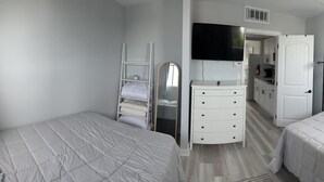 Un dormitorio con dos camas, un aparador, un televisor y una puerta que da a un baño.