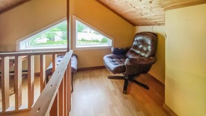 Une chambre à coucher aménagée dans un espace de type « loft », avec un plafond en bois, une fenêtre, un fauteuil en cuir marron et une rambarde en bois.