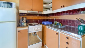 Une cuisine de taille réduite, équipée d’un réfrigérateur, d’une cuisinière, d’un évier et de meubles de rangement en bois.
