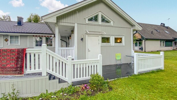 Une maison à deux étages avec un porche à l’avant, un petit garage attenant et un espace extérieur aménagé pour s’asseoir.