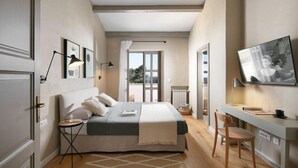 Un dormitorio con cama, mesitas de noche, escritorio, silla, televisor y vistas al exterior.