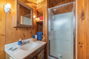 A wooden bathroom with a white sink, a mirror, and a frosted glass shower door. - Charming Cottage on the Bay and Golf Course with private patio and boat dock. (Sodus Point)