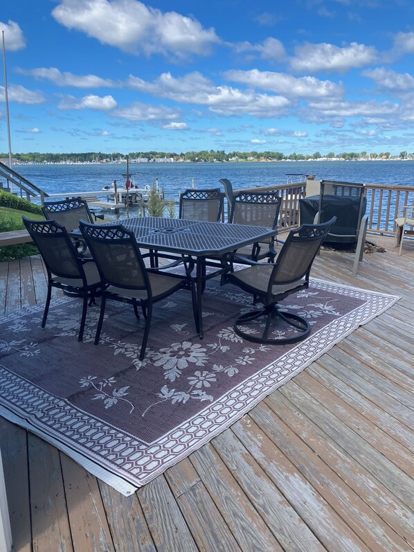 A wooden deck with a table and chairs, overlooking a body of water. - Charming Cottage on the Bay and Golf Course with private patio and boat dock. (Sodus Point)