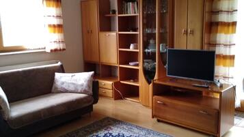 Ein Wohnzimmer mit einer Couch, einem Fernsehschrank, einem Holzschrank und einem gemusterten Teppich.