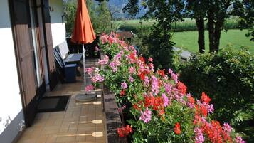 Eine Terrasse mit Fliesenboden, einer Holzbank, einem Tisch und einem orangefarbenen Sonnenschirm.
