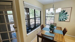 A dining area with a wooden table, chairs, a chandelier, and a large window with blinds. - Mountain View, Resort Style Condo (Tucson)