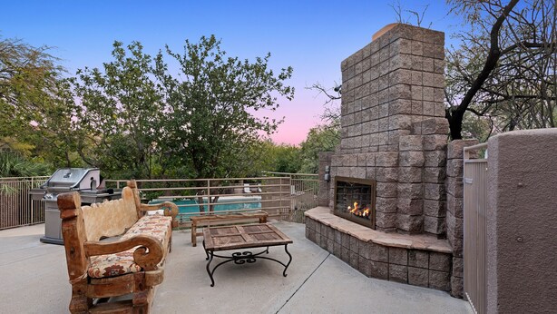 An outdoor patio with a stone fireplace, a wooden bench, a table, and a pool in the background. - Mountain View, Resort Style Condo (Tucson)