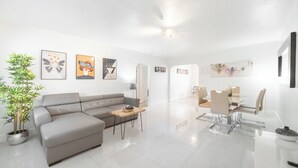 Ein modernes Wohnzimmer mit einem grauen Sofa, einem Holztisch und einem Essbereich mit weißem Tisch und Stühlen.
