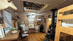 L’intérieur chaleureux d’un chalet avec un plancher en bois, un coin repas, des lits superposés et un ventilateur de plafond.