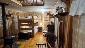Un intérieur de chalet chaleureux avec un lit en mezzanine, des murs en bois, une cheminée et un coin repas.