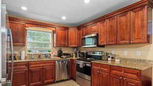 A kitchen with wooden cabinets, stainless steel appliances, granite countertops, and a window with blinds.