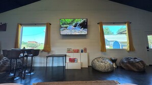 Ein gemütliches Wohnzimmer mit Fernseher an der Wand, einer Bar und großen Fenstern mit Vorhängen.