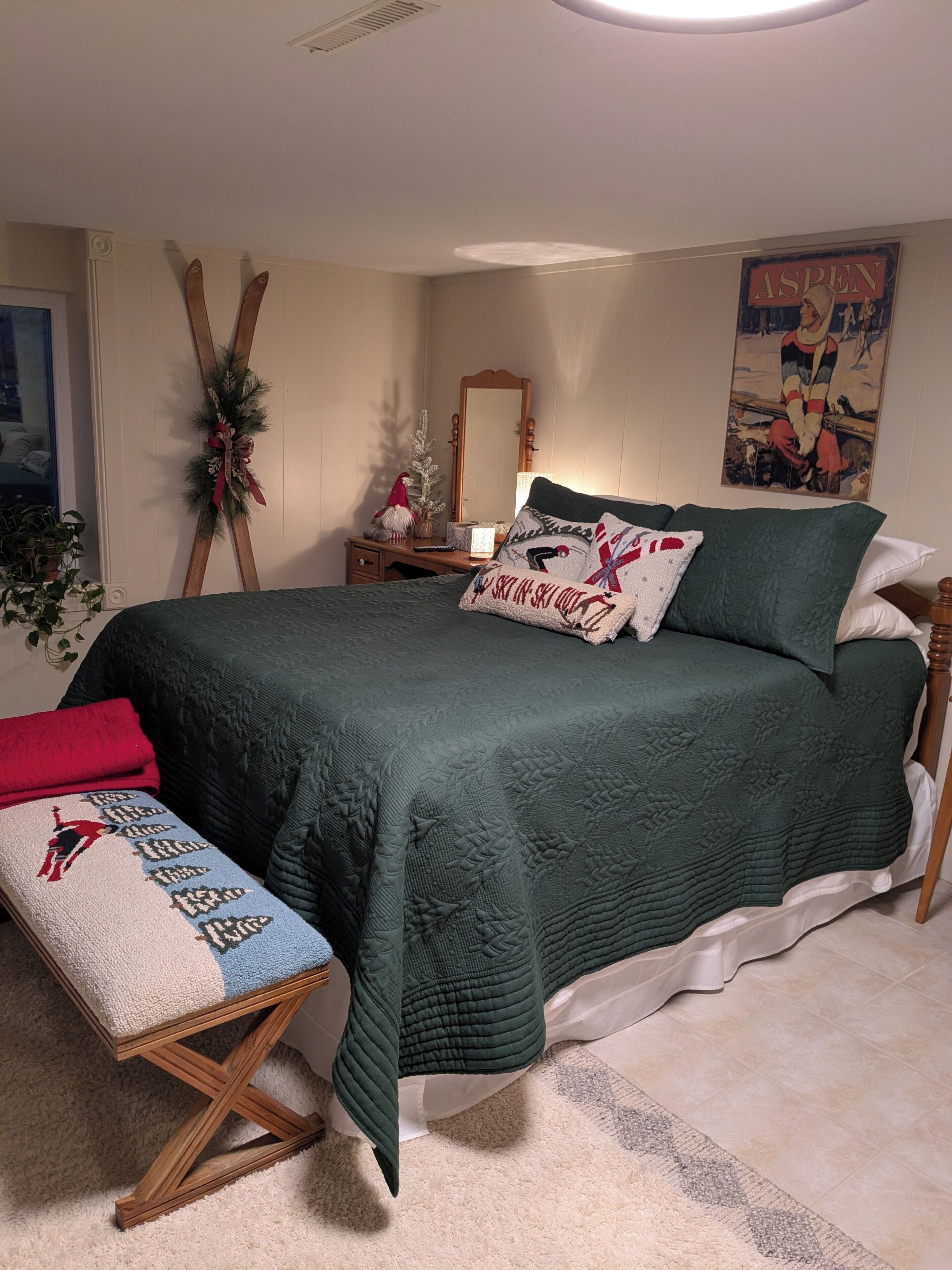 A bedroom with a bed, a bench, a mirror, a wall decoration, and a window.