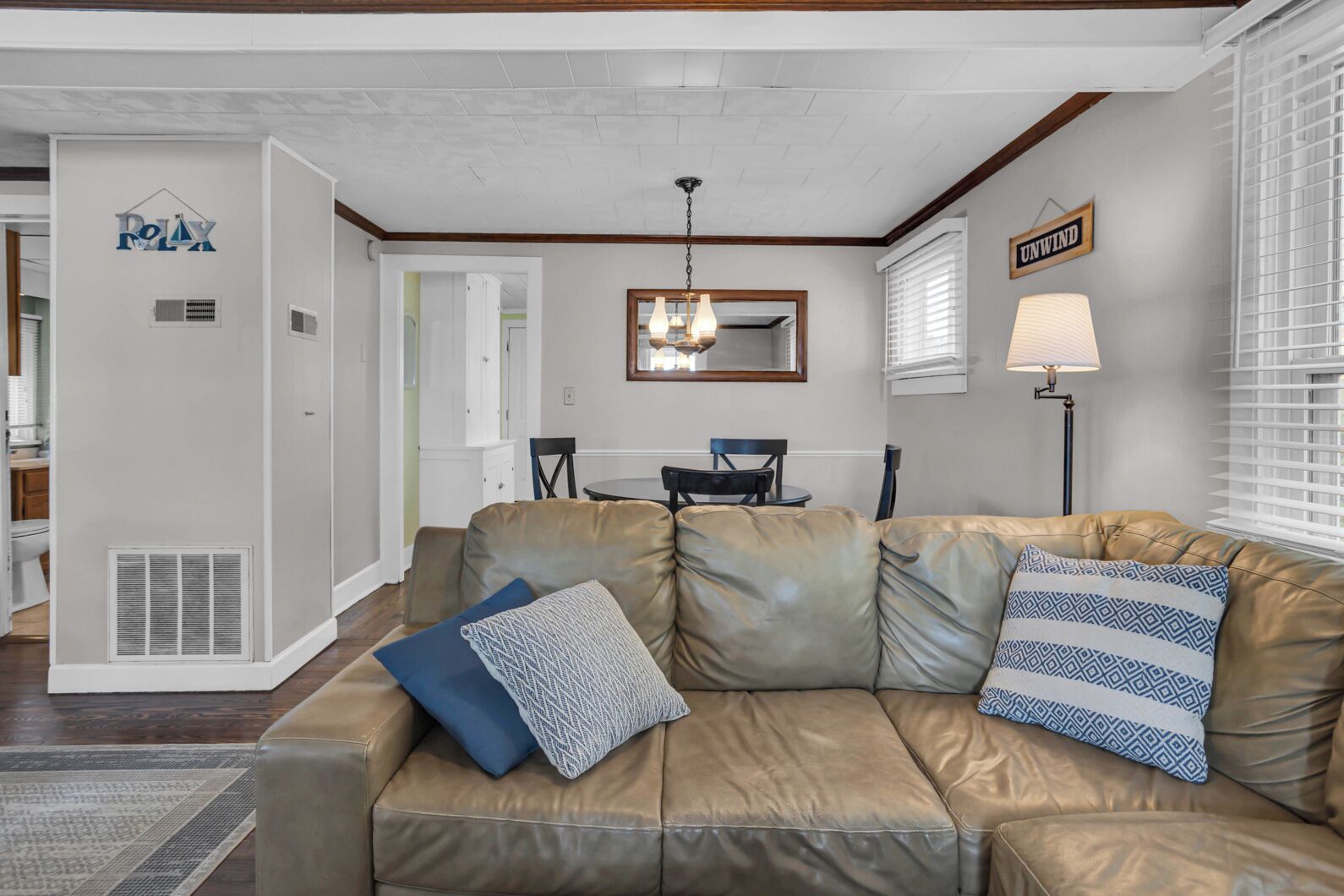 A living room with a beige leather sofa, a chandelier, a dining table with chairs, and a sign that reads "UNWIND".