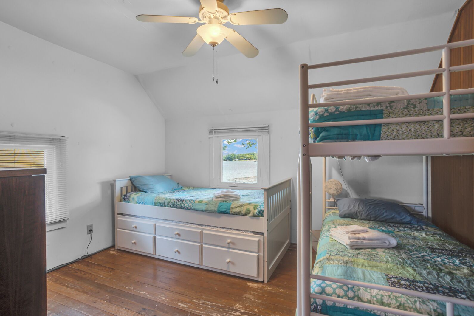 Un dormitorio con una cama litera, una cama individual, un ventilador de techo y una ventana con persianas.