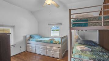 Un dormitorio con una cama litera, una cama individual, un ventilador de techo y una ventana con persianas.