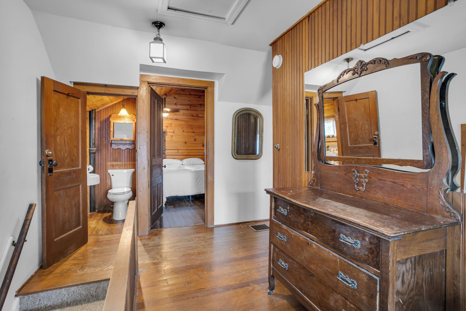 A wooden interior with a large mirror, a wooden dresser, and a bathroom visible through an open door.