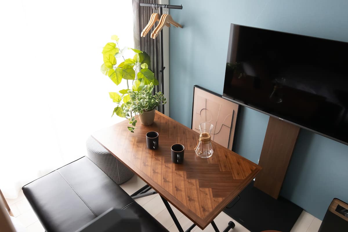 Una sala de estar moderna con una mesa de madera, dos tazas negras, un recipiente de vidrio y una planta en maceta.