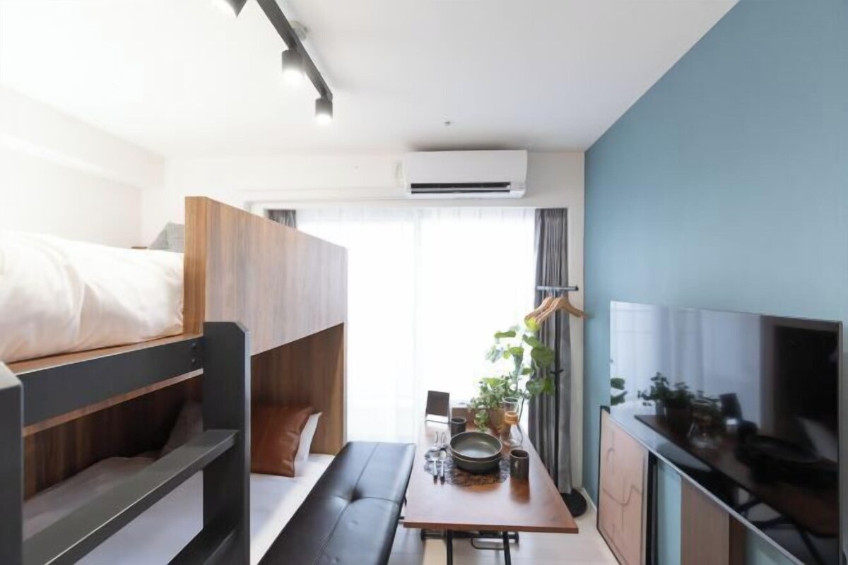A compact hotel room with a bunk bed, a small dining table, a TV, and a kitchenette.