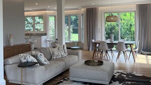 A modern living room with a sectional sofa, a dining area with a table and chairs, and a kitchen in the background.