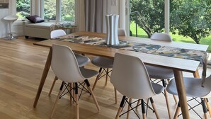 A modern dining area with a wooden table, white chairs, and a hanging light fixture.