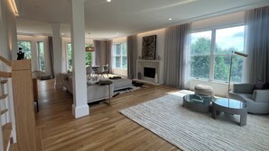 A spacious living room with a fireplace, large windows, and a dining area.
