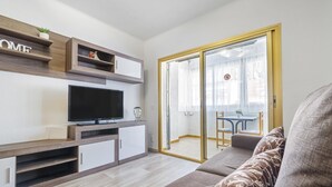 A modern living room with a flat-screen TV, built-in shelving, and a sliding glass door leading to a balcony. - Ground floor with pool and parking 100m beach (Cambrils)