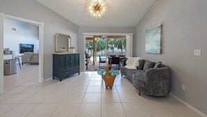 Uma sala de estar espaçosa com um sofá cinza, uma mesa de centro de vidro e um lustre moderno.