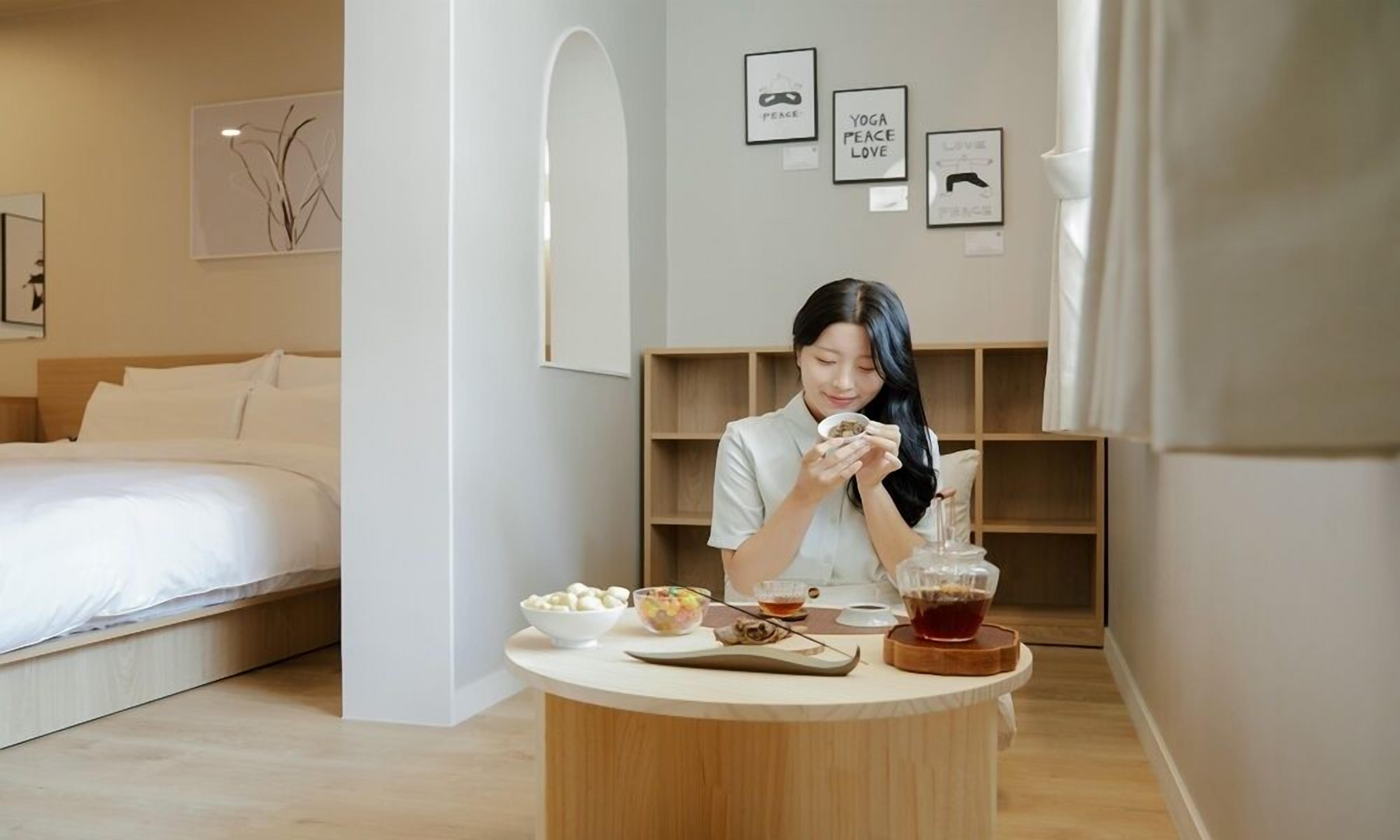 Una camera d'albergo moderna con un letto rifatto, un tavolo rotondo con cibo e bevande, e un'arredamento minimalista con citazioni motivazionali incorniciate al muro.