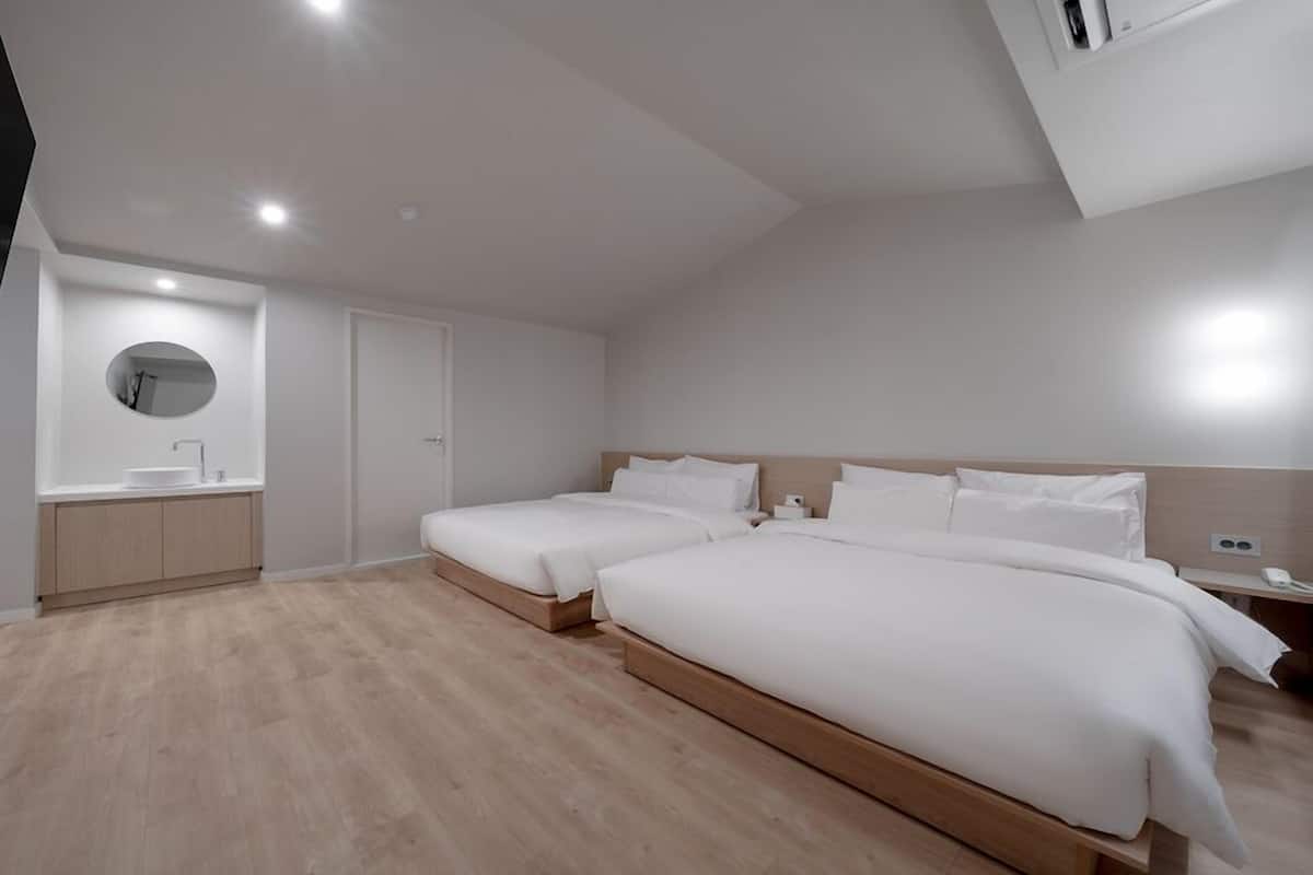 A modern hotel room with two single beds, a small bathroom with a sink, and a TV mounted on the wall.