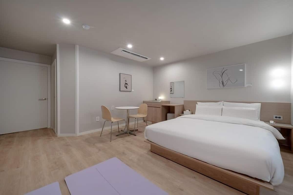A modern hotel room with a large bed, a desk, a chair, and a small table.