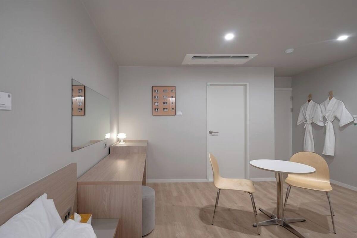 A modern hotel room with a bed, a desk, a chair, and a small table.