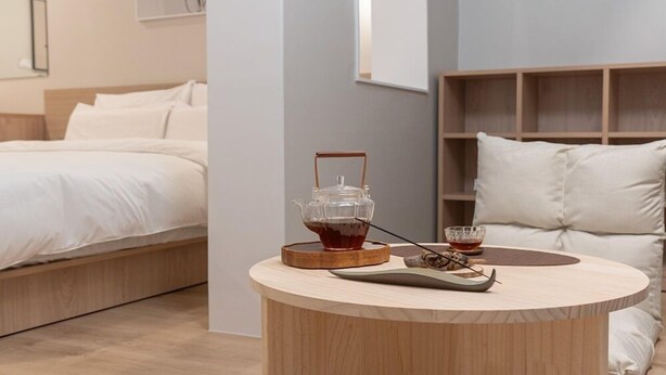A modern bedroom with a bed, a bedside table with a glass teapot, and a small table with a cup and saucer. - ANNK HOTEL CHEONAN SEONGJEONG (Cheonan)