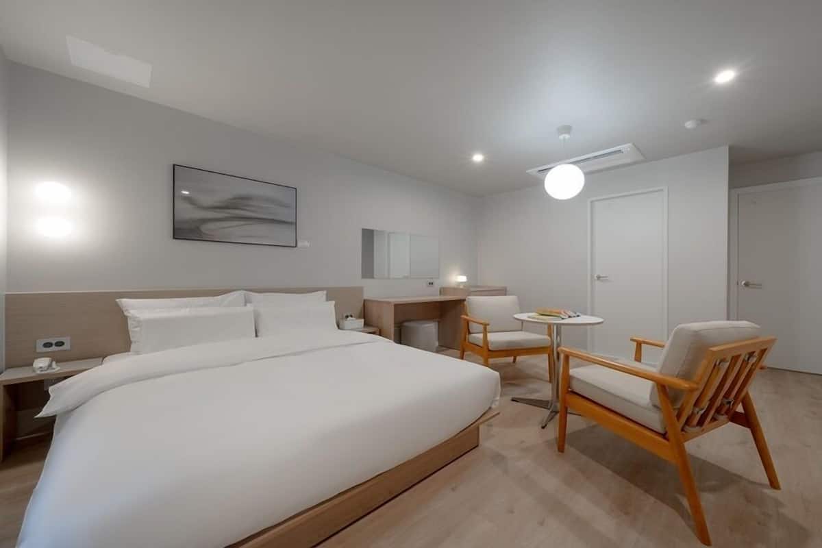A modern hotel room with a large bed, a desk, a chair, and a small table.